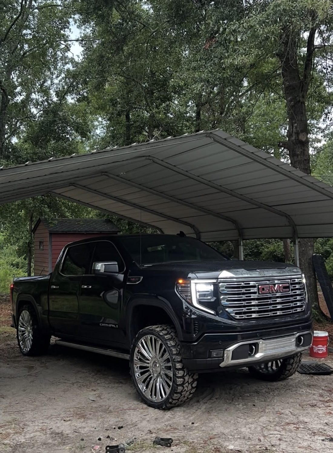 Black GMC Denali with a chrome grille and polished wheels under a metal carport