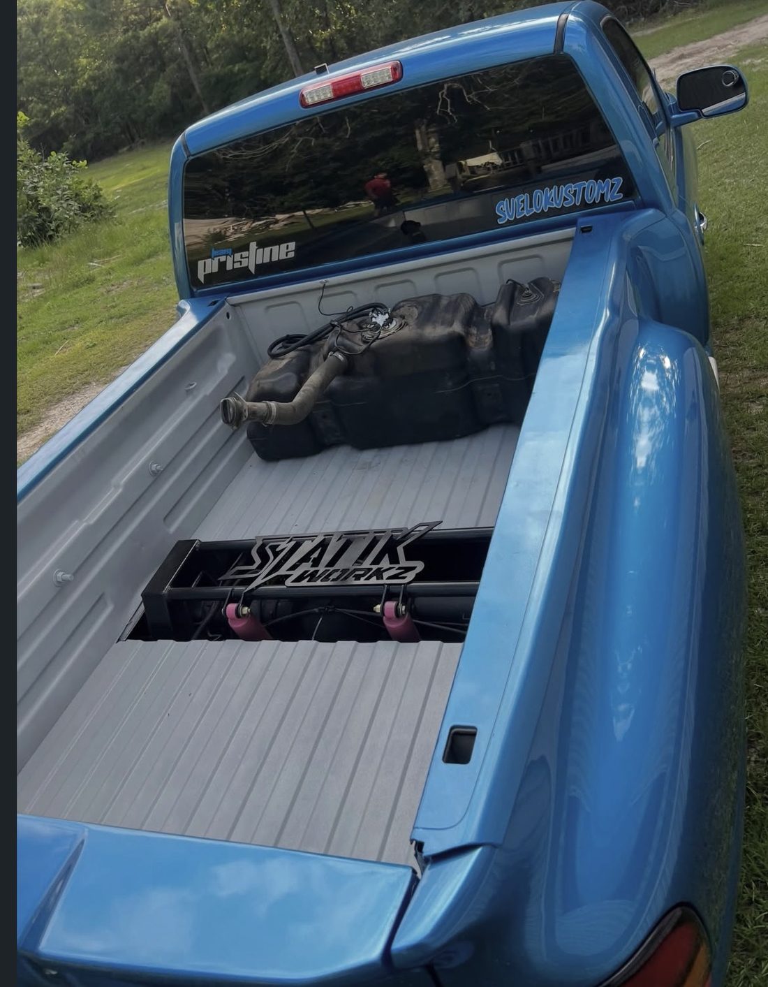 Blue pickup seen from behind, with a section cut out of the bed floor and a frame visible underneath