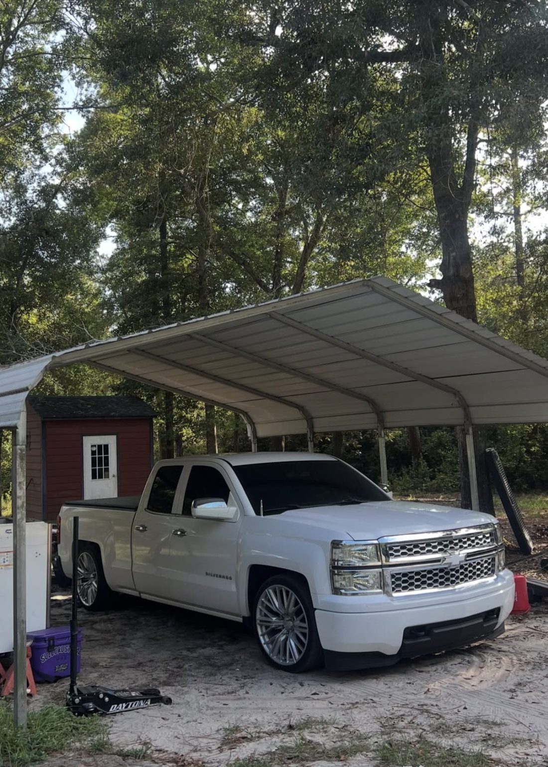 White Chevrolet Silverado sitting low on large silver wheels under a metal carport